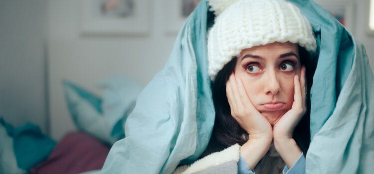 Repair Request Rumble Image of woman bundled up in a woolly hat and comforter waiting for heater to be repaired