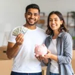 Image of happy couple moving in to an apartment holding money and a piggy bank to show they are saving money with new California security deposit laws