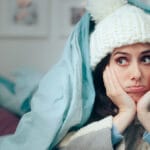 Image of woman bundled up in a woolly hat and comforter waiting for heater to be repaired