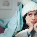 Image of woman bundled up in a woolly hat and comforter waiting for heater to be repaired