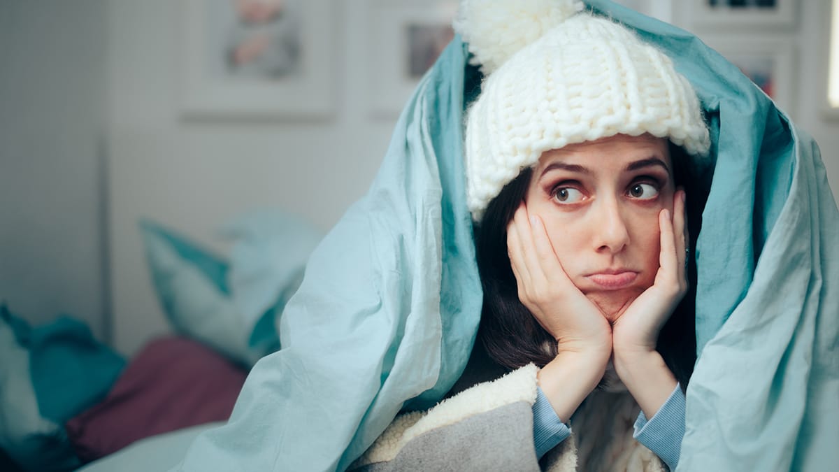 Image of woman bundled up in a comforter and hat due to no heat, repair request